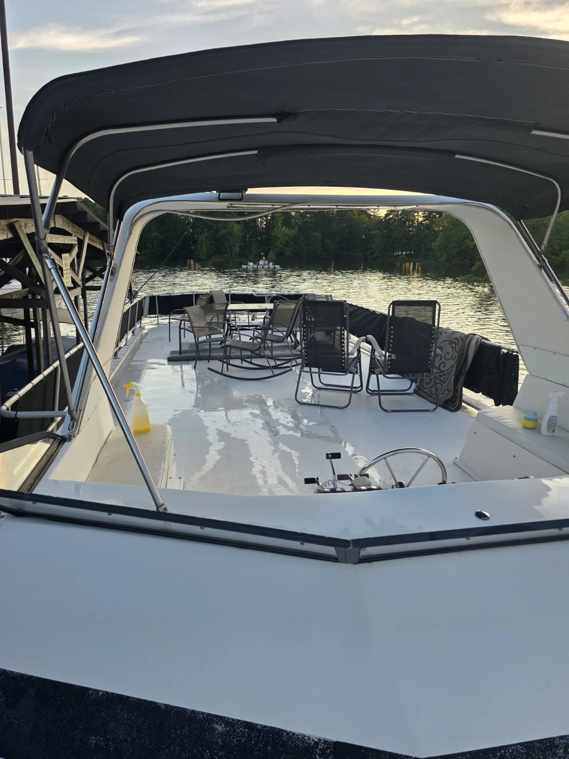 Houseboat deck with chairs, wet flooring and cleaning supplies beneath a black canopy
