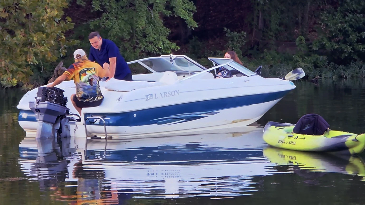 People gathered around an exposed boat motor on the water beside a kayak